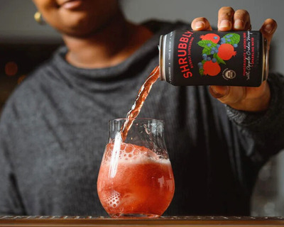 a woman pouring pomegranate aronia berry shrubbly into a glass